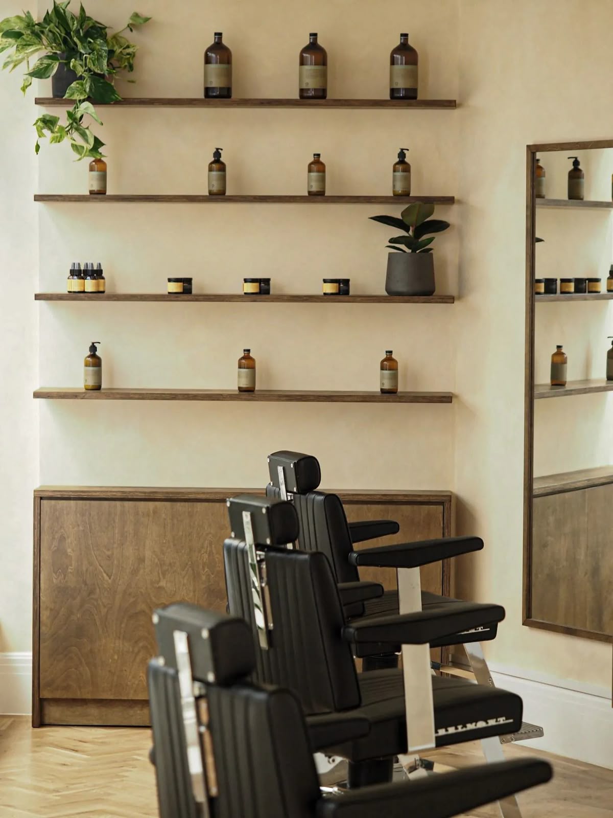Modern barbershop interior with dark shelves, amber product bottles, and black leather chairs