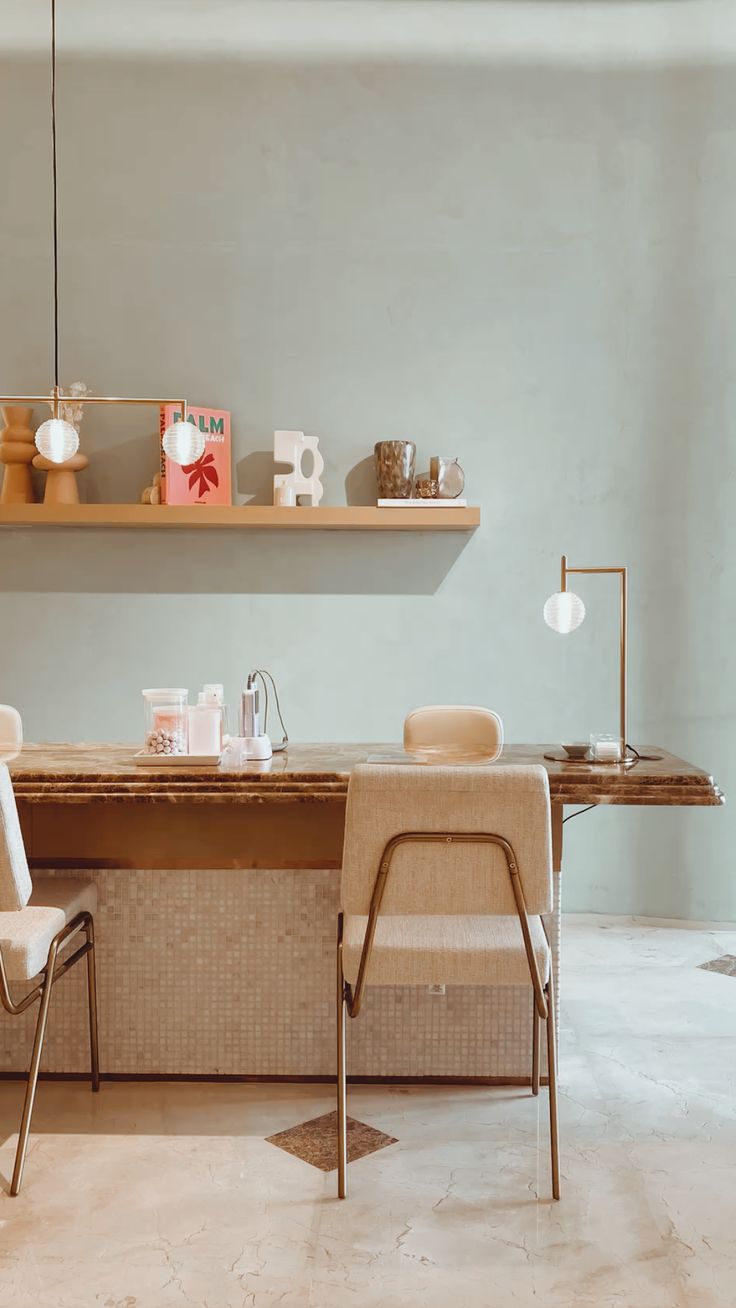 Elegant nail station with sage green walls, marble countertop, modern chairs and warm lamp lighting