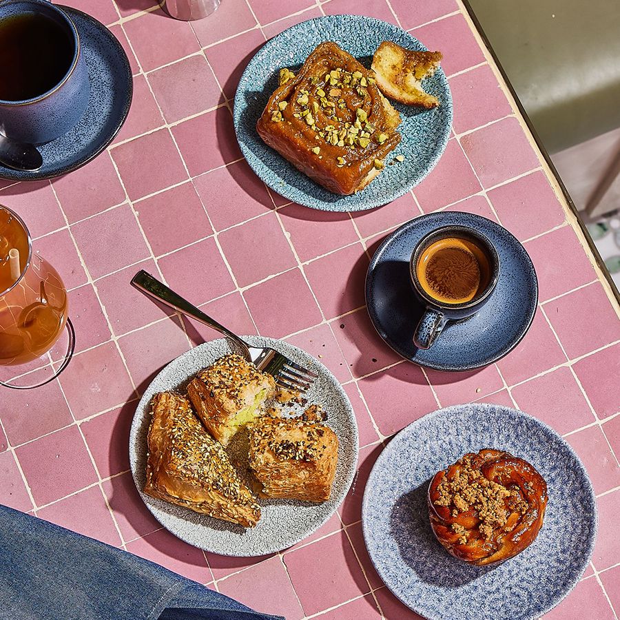 Golden pastries on blue plates with espresso and iced drinks in warm morning light