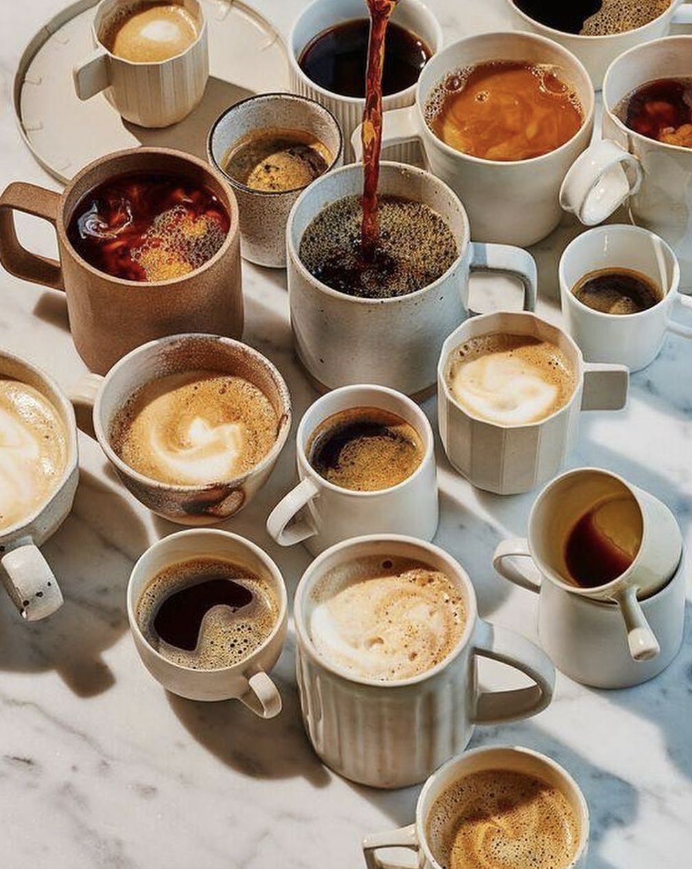 Collection of artisanal coffee cups with various ceramic mugs on marble surface