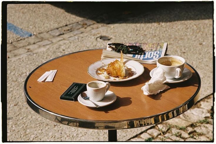Parisian cafe table with croissant, coffees, and newspaper in warm morning light